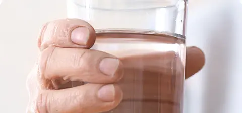 Person&rsquo;s hand holding a glass of clear liquid